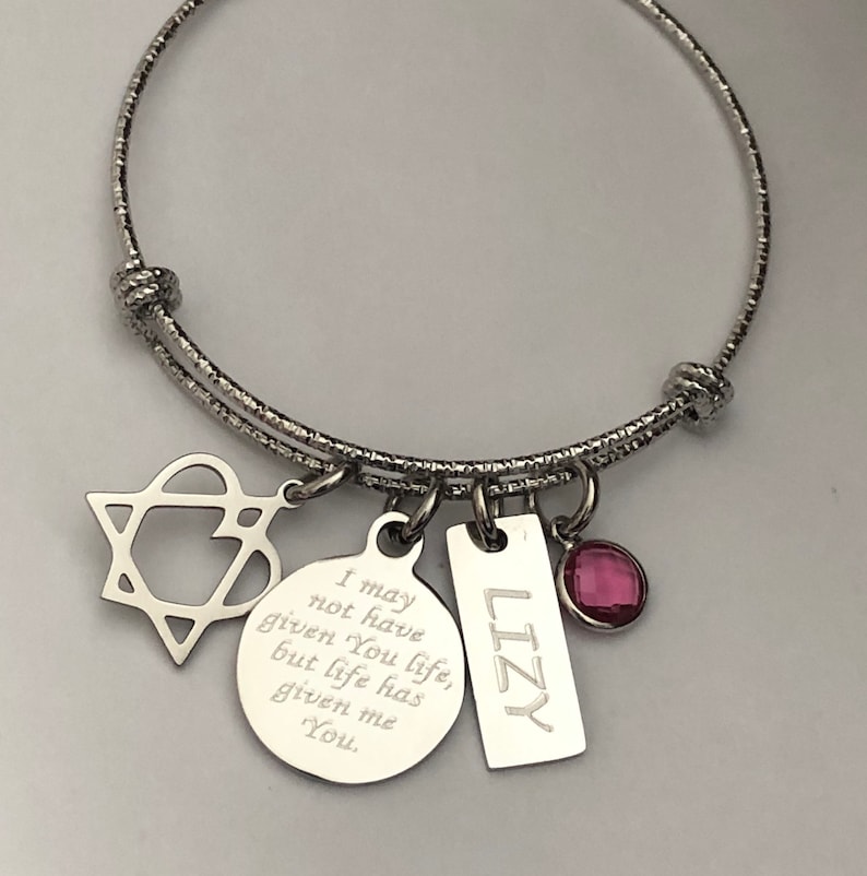 May include: Silver charm bracelet with a star, heart, round charm with the text "I may not have given You life, but life has given me You." and a rectangular charm with the text "LIZY". The bracelet also has a pink gem.