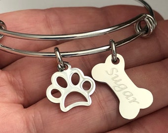May include: Silver expandable bracelet with two charms: a paw print and a bone engraved with the name "Sugar".
