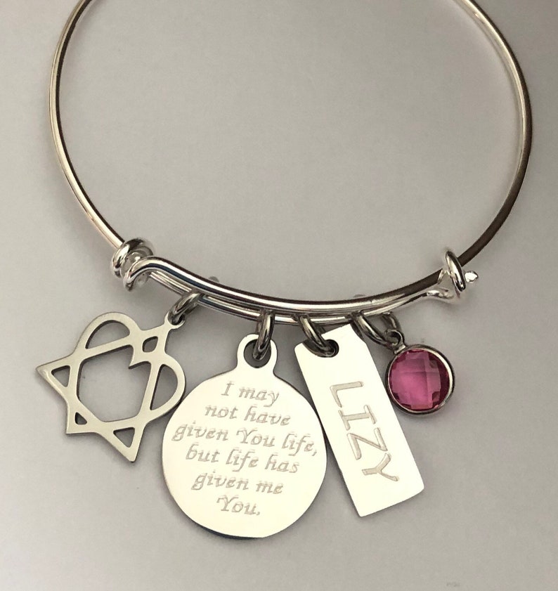 May include: Silver charm bracelet with a heart, a round charm with the text "I may not have given You life, but life has given me You", a rectangular charm with the text "LIZY", and a pink crystal charm.