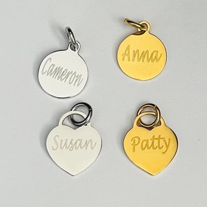May include: Four personalized name tags, two round and two heart-shaped. The round tags are silver and gold with the names "Cameron" and "Anna" engraved on them. The heart-shaped tags are also silver and gold with the names "Susan" and "Patty" engraved on them.