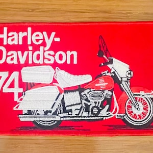 May include: Red rectangular patch featuring a Harley-Davidson motorcycle design. The patch includes the words "Harley-Davidson" in white, along with the number "74". The motorcycle is red, white, and black.