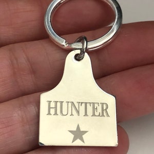 May include: Silver keychain with a star and the name "HUNTER" engraved on a tag shaped like a cattle ear tag.