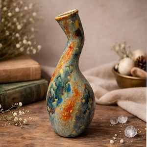 Può includere: Un vaso in ceramica fatto a mano con un collo curvo unico. Il vaso presenta una miscela di colori, tra cui blu, arancione e giallo, creando un aspetto strutturato e artistico. È un oggetto decorativo, adatto per esporre fiori.