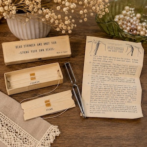 May include: A bead stringer and knot tier tool set including a cardboard box, two spools of thread labeled coarse and fine, and a metal knotting tool. An instruction sheet with text and diagrams is included for the bead stringing process.