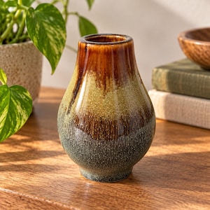 May include: A ceramic vase with a bulbous shape and a glossy finish. The glaze features a gradient of colours, transitioning from a deep brown at the rim to a mottled olive green in the centre, and ending in a dark, textured blue-grey at the base.