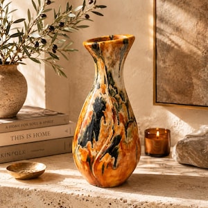 May include: A tall ceramic vase with a flared rim and a tapered neck, featuring a glossy glaze in shades of amber, burnt orange, and deep forest green with vertical drip patterns that create a textured, multi-colored appearance throughout.