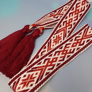 May include: A white and red woven belt with a geometric pattern and two burgundy tassels.