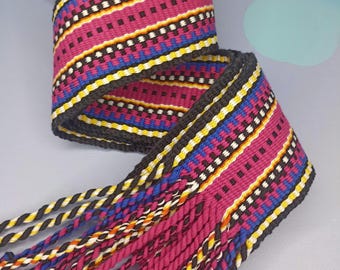 Può includere: Nastro tessuto con un motivo geometrico nei toni del rosa, nero, giallo, blu e bianco. Il nastro ha un bordo grigio scuro e nappe intrecciate nei colori coordinati. Adatto per artigianato o decorazioni.