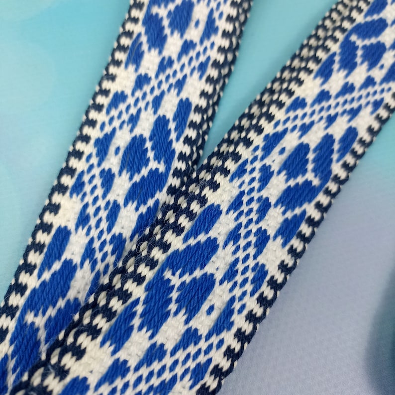 K&ouml;nnte beinhalten: Nahaufnahme eines gewebten Stoffbandes mit wei&szlig;em Hintergrund und einem sich wiederholenden Muster aus blauen und schwarzen geometrischen Formen.
