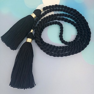 以下が含まれることがあります： 黒いロープベルトに黒いタッセルが2つ付いている。タッセルには金色のアクセントがある。