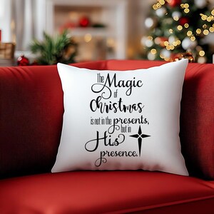 May include: White throw pillow with black text that reads "The Magic of Christmas is not in the presents, but in His presence." A star with a cross is above the word "His".