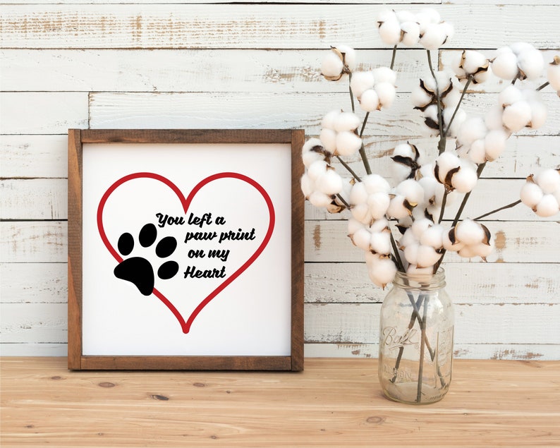 May include: A white wooden sign with a red heart and a black paw print. The sign says "You left a paw print on my heart".