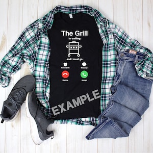 May include: A black t-shirt with a white graphic of a grill with the text "The Grill is calling and I must go". The graphic also includes a phone icon with the options "Decline" and "Accept".
