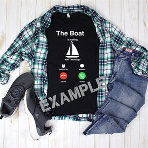 Può includere: Maglietta nera con una grafica bianca di uno schermo di telefono. Il testo sullo schermo recita "The Boat is calling and I must go". Lo schermo del telefono mostra un'icona di una barca a vela e tre pulsanti: "Remind Me", "Message", "Decline" e "Accept".