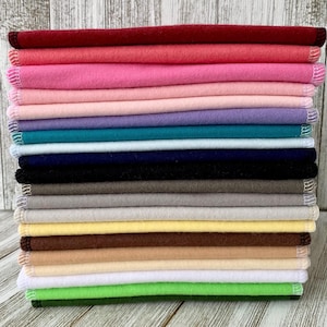 Könnte beinhalten: Ein Stapel von 18 Stoffquadraten in verschiedenen Farben, darunter Rot, Rosa, Hellblau, Türkis, Marineblau, Schwarz, Grau, Beige, Braun, Gelb, Weiß und Grün. Die Stoffquadrate sind ordentlich gestapelt und haben einen fertigen Rand.