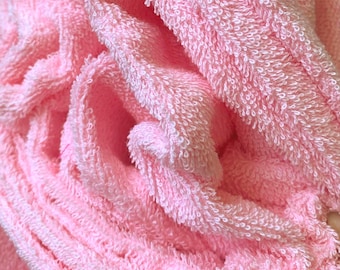 Può includere: Primo piano di un morbido asciugamano in spugna rosa. L'asciugamano è piegato e ha una superficie strutturata con anelli visibili. Il colore è un rosa pastello chiaro e il tessuto appare morbido e assorbente.