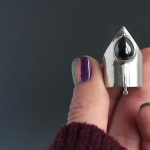 May include: A silver ring with a black gemstone set in a pointed, triangular design.