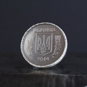 May include: A silver coin ring featuring a Ukrainian coin. The coin has the word "Україна" at the top, a coat of arms in the center, and the year 2014 at the bottom. The ring has a textured edge.