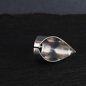 May include: A silver ring with a teardrop-shaped design. The ring is open on one side and has a smooth, polished finish.
