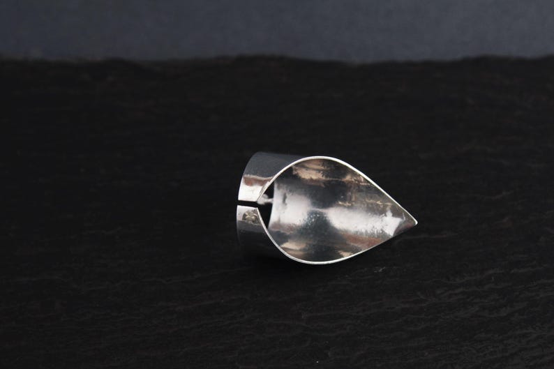 May include: A silver ring with a teardrop-shaped design. The ring is open on one side and has a smooth, polished finish.