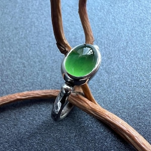 May include: A silver ring with a green oval gemstone set in a bezel setting. The ring has a textured band and small silver accents.
