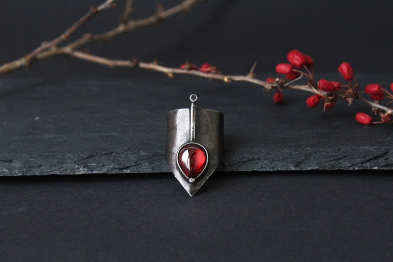 May include: A silver ring with a pointed design and a red gemstone in the center.