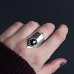 May include: A silver ring with a black gemstone set in a geometric design.