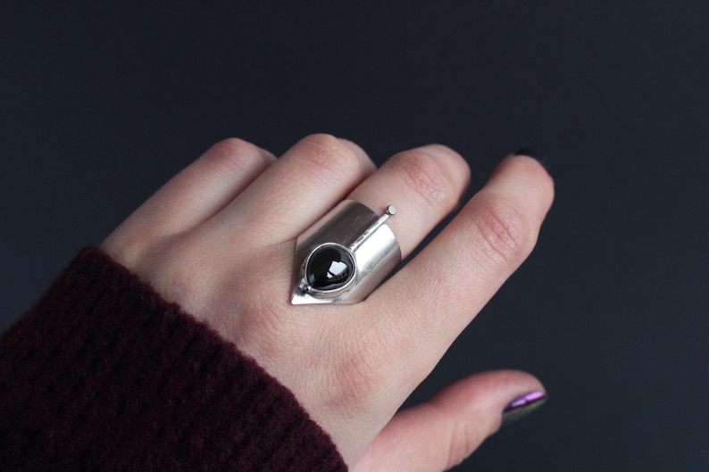 May include: A silver ring with a black gemstone set in a geometric design.