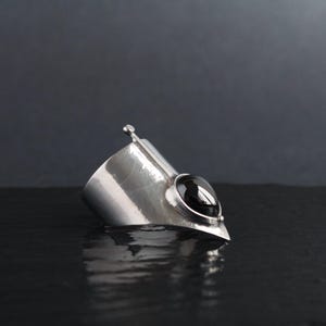 May include: A silver cuff bracelet with a black gemstone. The bracelet is designed with a pointed tip and a hammered texture.