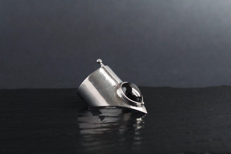 May include: A silver cuff bracelet with a black gemstone. The bracelet is designed with a pointed tip and a hammered texture.