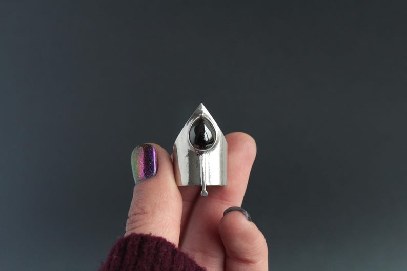 May include: A silver ring with a black gemstone set in a pointed, triangular design.