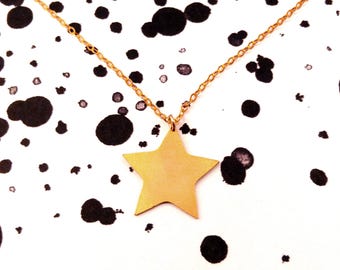 May include: A gold chain necklace with a large gold star pendant. The necklace is photographed on a white background with black splatter paint.