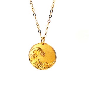 May include: A gold chain necklace with a round pendant featuring a detailed embossed design of a wave.