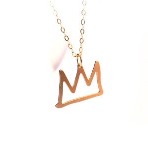 May include: A gold chain necklace with a simple crown pendant. The crown is a thin, outlined shape.