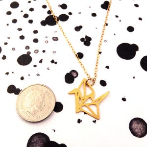 May include: Gold origami crane necklace pendant on a delicate chain. The pendant is about the size of a US quarter.