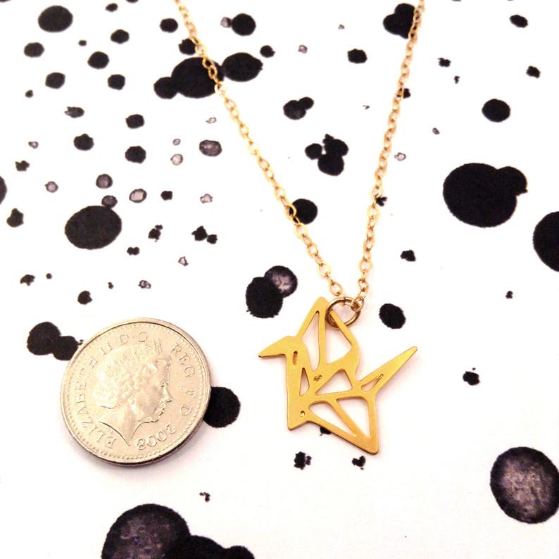 May include: Gold origami crane necklace pendant on a delicate chain. The pendant is about the size of a US quarter.