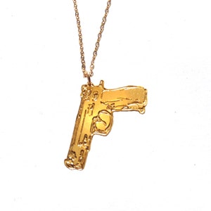 Pode incluir: Um colar dourado com um pingente em forma de pistola.