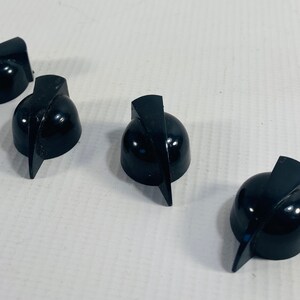 May include: Four black plastic knobs with a pointed, angled design. The knobs are used for adjusting volume or other settings on electronic devices.