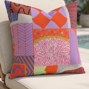 May include: A decorative pillow with a patchwork design. The pillow features a variety of geometric patterns in shades of orange, purple, pink, and blue. The pillow is resting on a beige lounge chair.