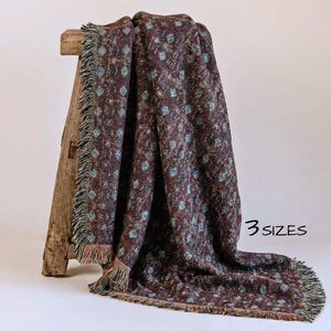 May include: A burgundy throw blanket with a repeating floral pattern in light blue and white. The blanket has a fringed edge and is draped over a wooden stool. The text "3 sizes" is visible.