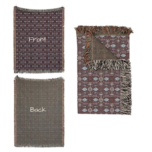 May include: Woven throw blanket with a geometric pattern in shades of burgundy, blue, and cream. The blanket has a fringed edge and the word "Front" is visible on one of the blankets. The back of the blanket is a solid brown color.