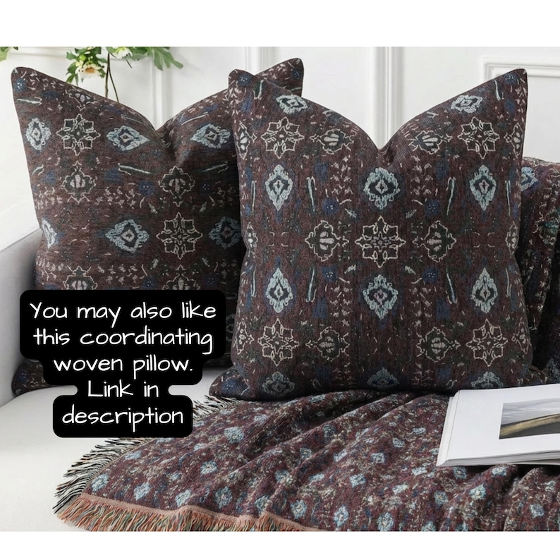 May include: Two decorative throw pillows with a dark brown background and a repeating pattern of white, blue, and teal shapes. A matching throw blanket with fringe is draped over a couch. Text on the image says, "You may also like this coordinating woven pillow. Link in description."