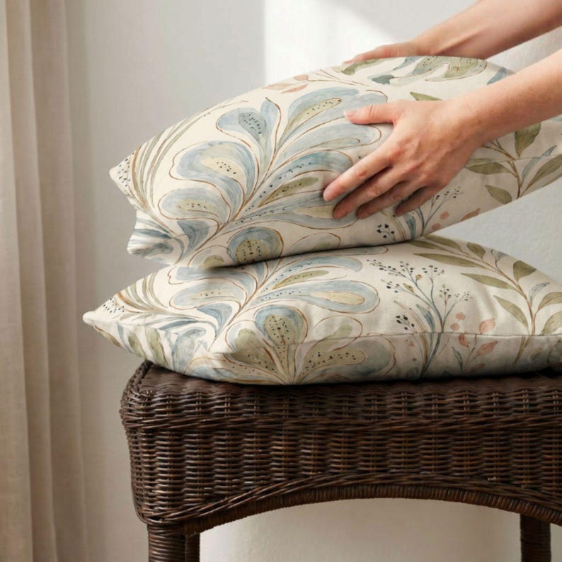 May include: Two rectangular throw pillows featuring a watercolour-style botanical print with large, flowing blue and green leaf patterns on an off-white background. The fabric displays soft, painterly brushstrokes and delicate stems.