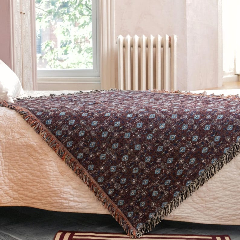 May include: A woven throw blanket with a repeating diamond pattern in shades of brown, blue, and cream. The blanket has a fringed edge and is draped over a bed. The blanket is approximately 60 inches by 50 inches.