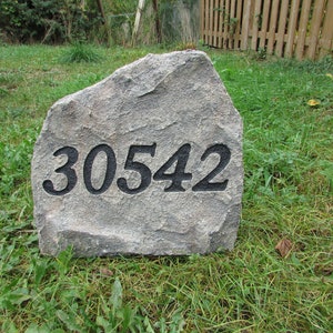 May include: A gray, textured stone with the number "30542" carved in black. The stone is set in a grassy yard, suggesting a house number marker or garden feature.
