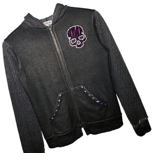 May include: Black zip-up hoodie with a skull graphic on the front. The hoodie has a gray knit trim and black studs on the pockets and sleeves.
