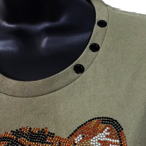 May include: A green t-shirt with a rhinestone tiger design. The shirt has a round neckline with black snap buttons.