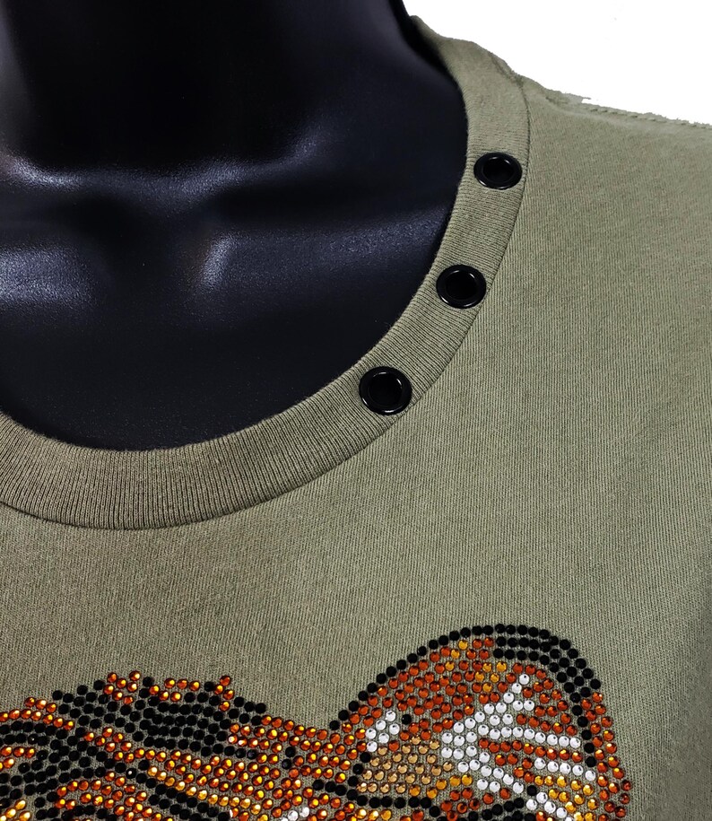 May include: A green t-shirt with a rhinestone tiger design. The shirt has a round neckline with black snap buttons.