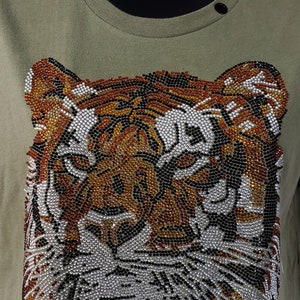 May include: A green t-shirt with a tiger face design made of rhinestones. The tiger's face is made of black, brown, and silver rhinestones.