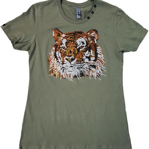 May include: A green t-shirt with a beaded tiger face design. The tiger's face is made of orange, brown, white, and black beads.